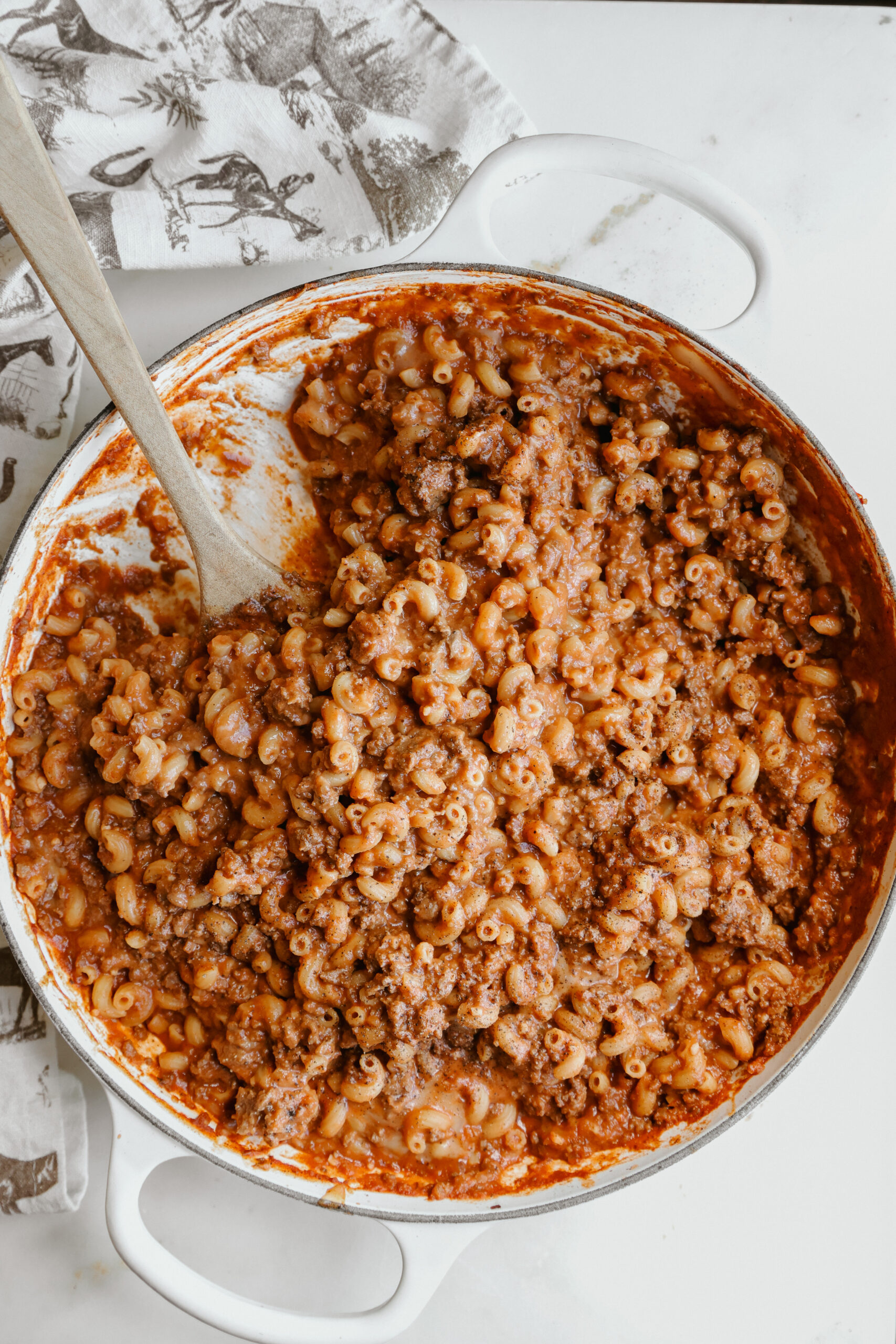 Chili mac without beans in a white cast iron braiser with a wooden spoon