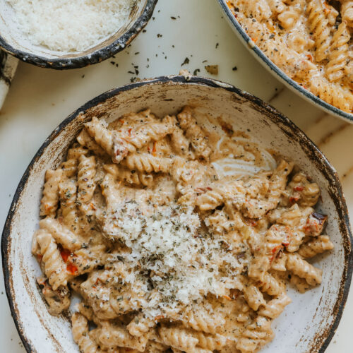 Creamy sun-dried tomato pasta in a bowl garnished with parmesan and herbs