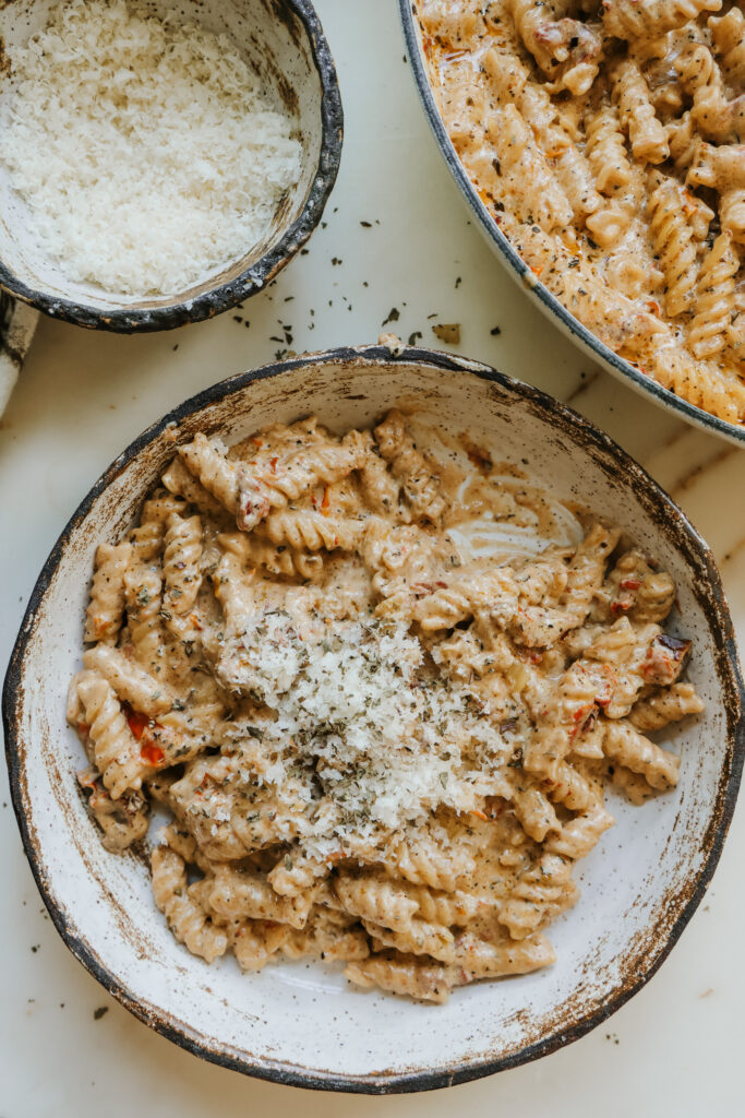Creamy sun-dried tomato pasta in a bowl garnished with parmesan and herbs