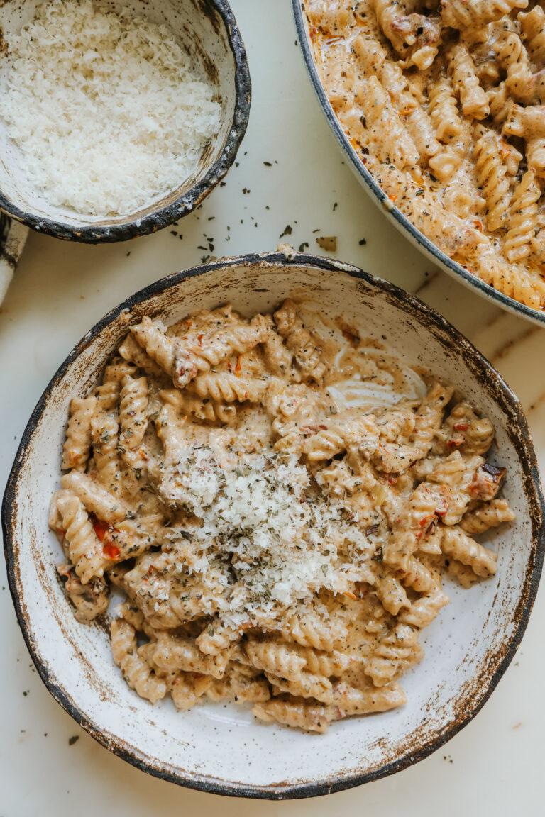 Creamy sun-dried tomato pasta in a bowl garnished with parmesan and herbs