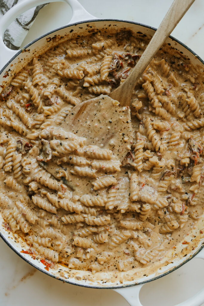 Close-up of creamy sun-dried tomato pasta with a wooden spoon