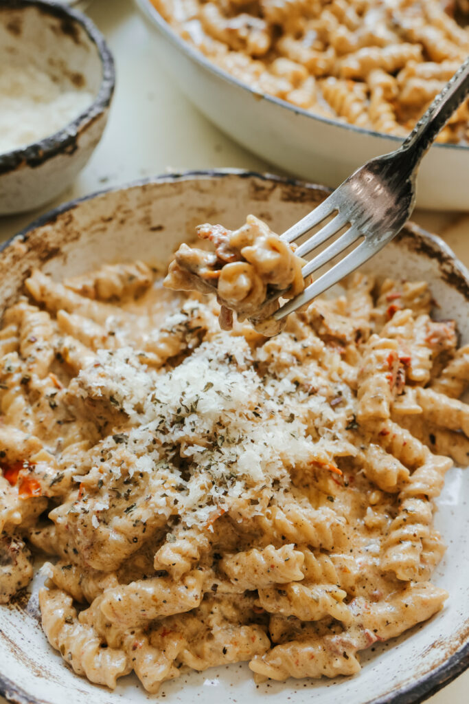 Forkful of creamy sun-dried tomato pasta lifted from the bowl