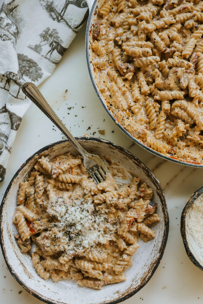 Bowl of creamy sun-dried tomato pasta topped with parmesan next to the skillet