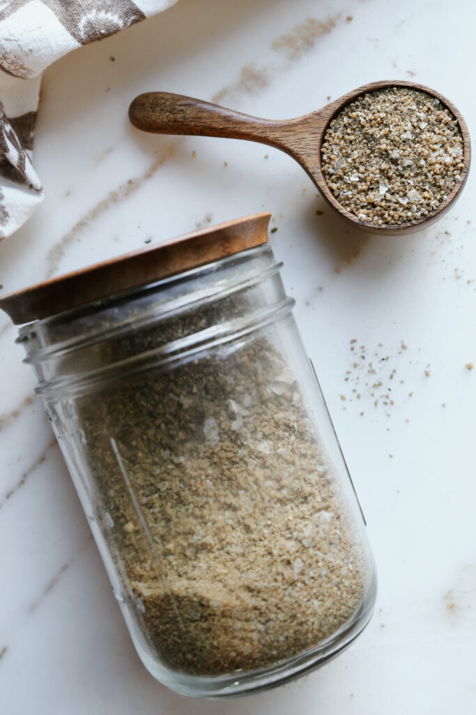 Homemade brown sugar salmon rub stored in a glass jar with a wooden lid next to a filled wooden scoop